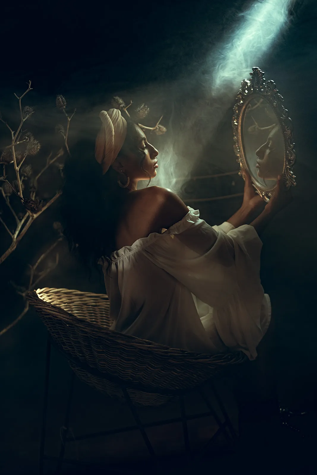 A woman in a white off-shoulder dress holds a gilded mirror into smoky light and studies her own reflection.