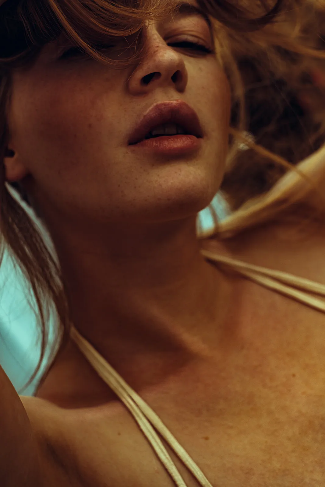 Close-up of a woman's face in warm backlight with windswept hair and slightly parted lips.