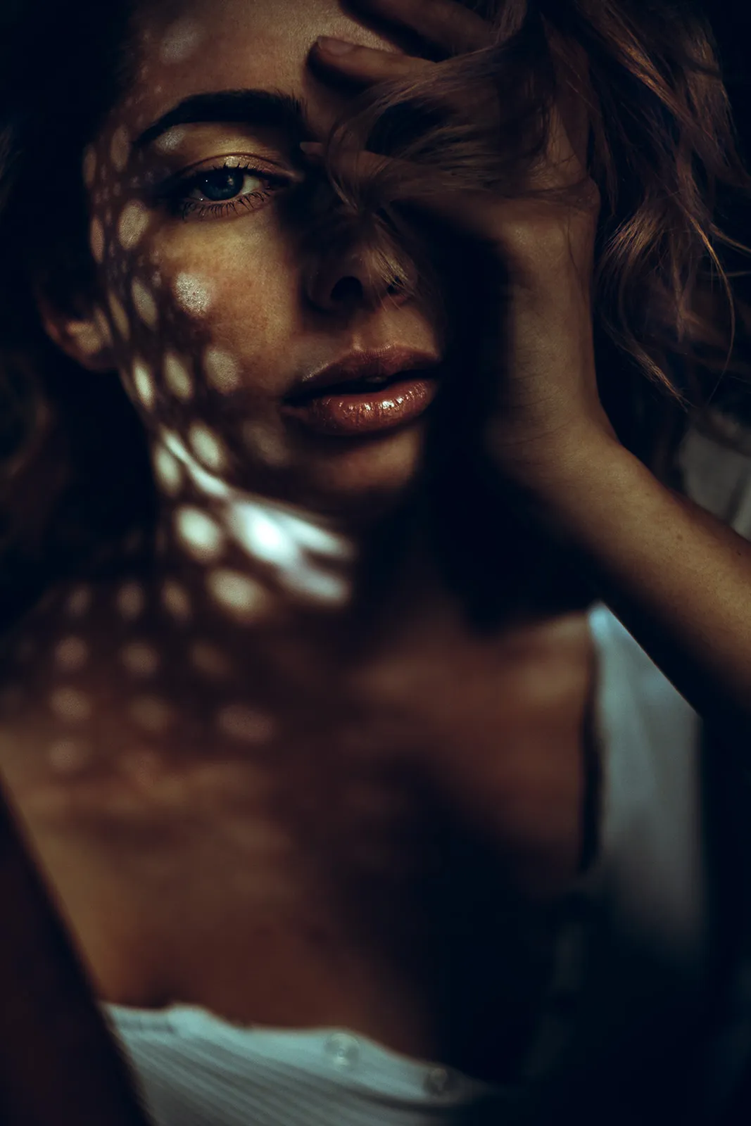 Dappled window light falls across a face while a hand rests against the forehead.