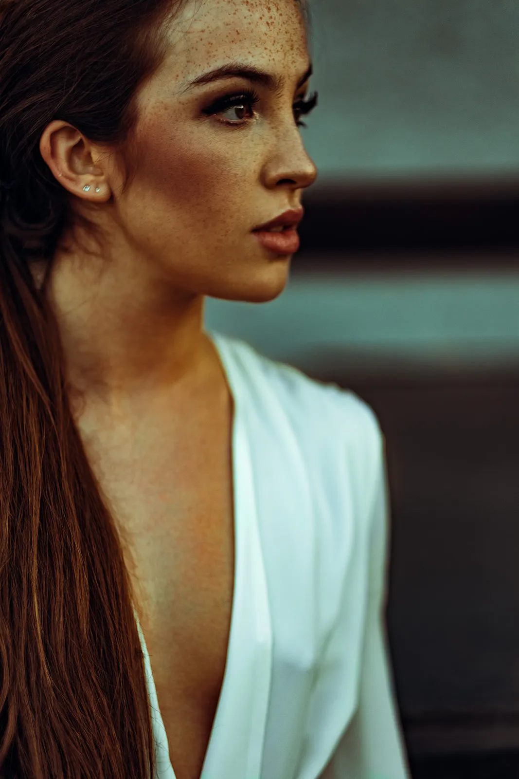 Side profile of a young freckled woman in warm backlight wearing a draped white garment.